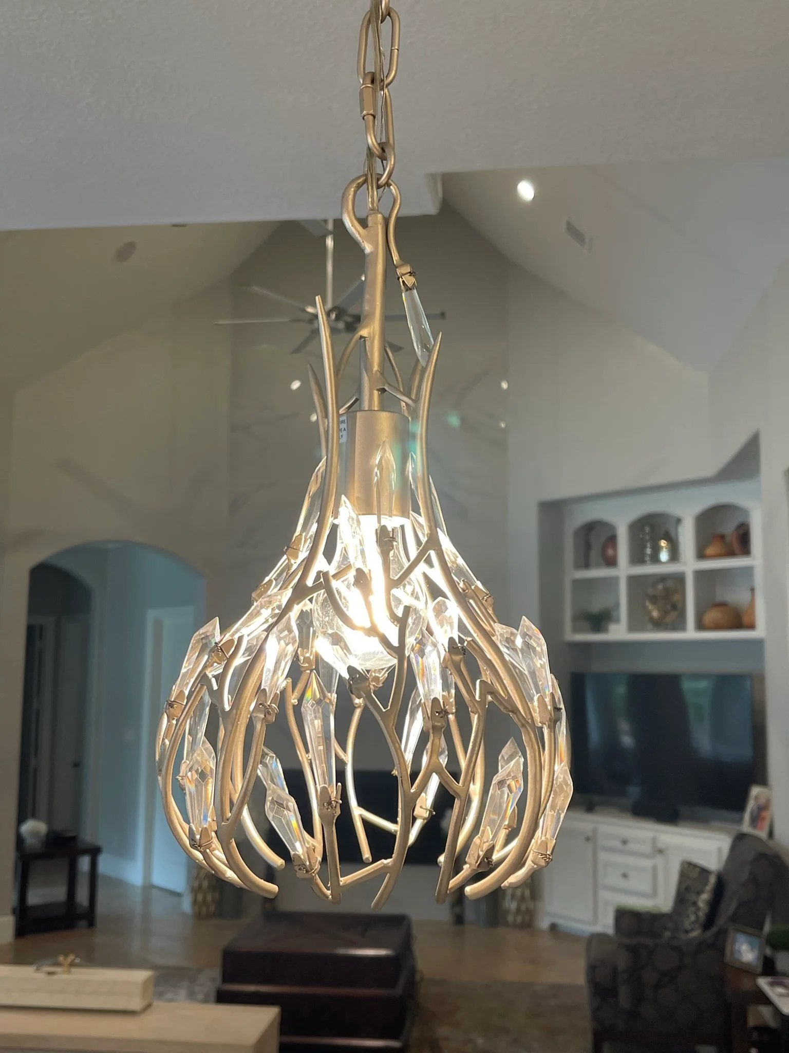 Brass and crystal pendant light with leaf-shaped accents hanging in residential great room