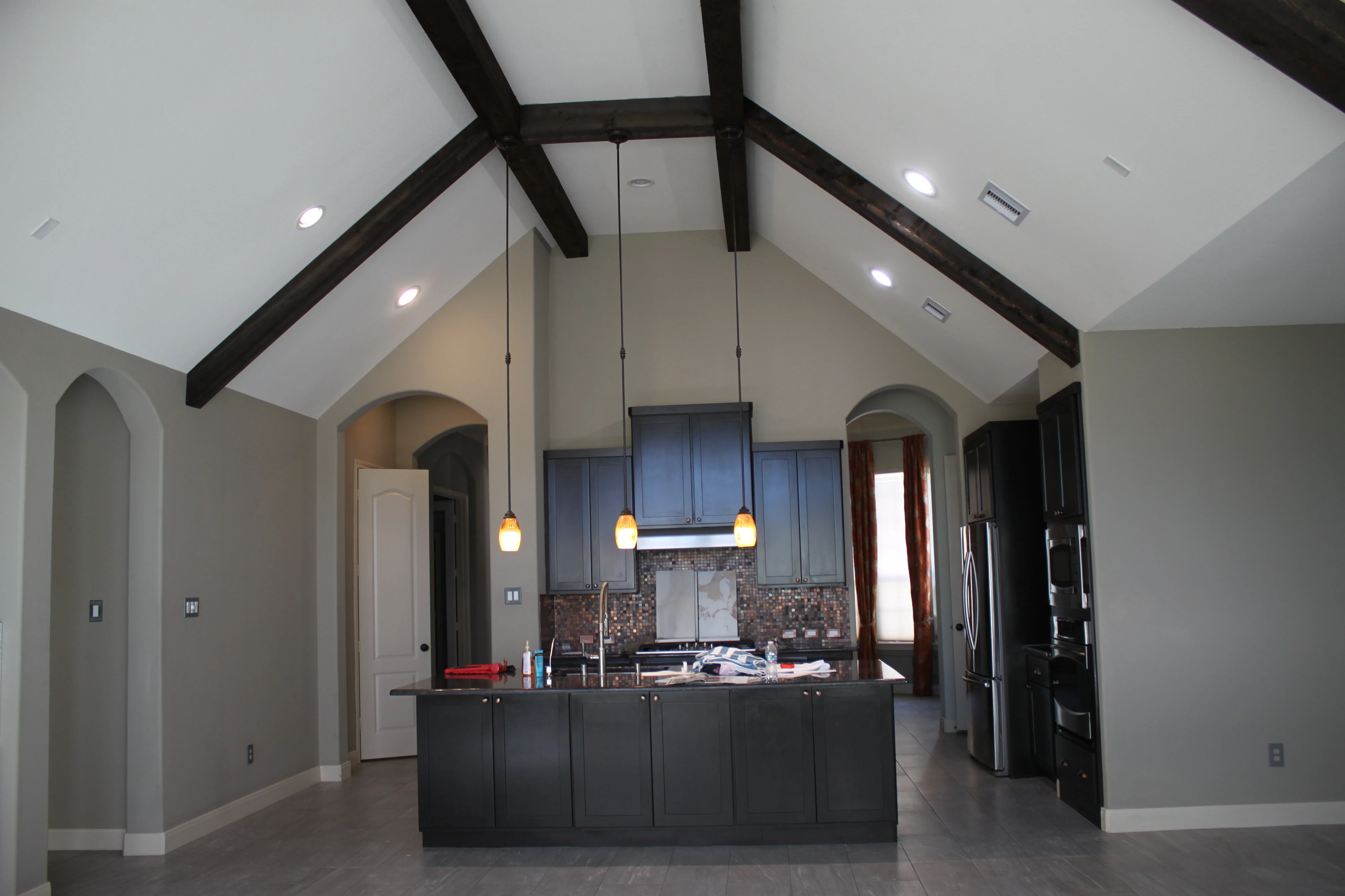 Modern kitchen with vaulted ceiling, dark beams, blue cabinetry, and mosaic backsplash