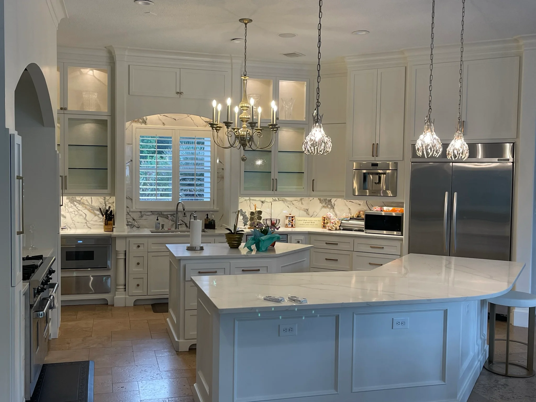 Luxury kitchen with white cabinetry, marble surfaces, stainless steel appliances, and pendant lighting