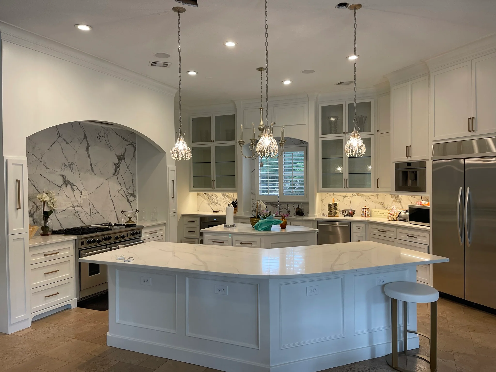 Modern luxury kitchen with white cabinetry, blue island, marble countertops, and pendant lighting