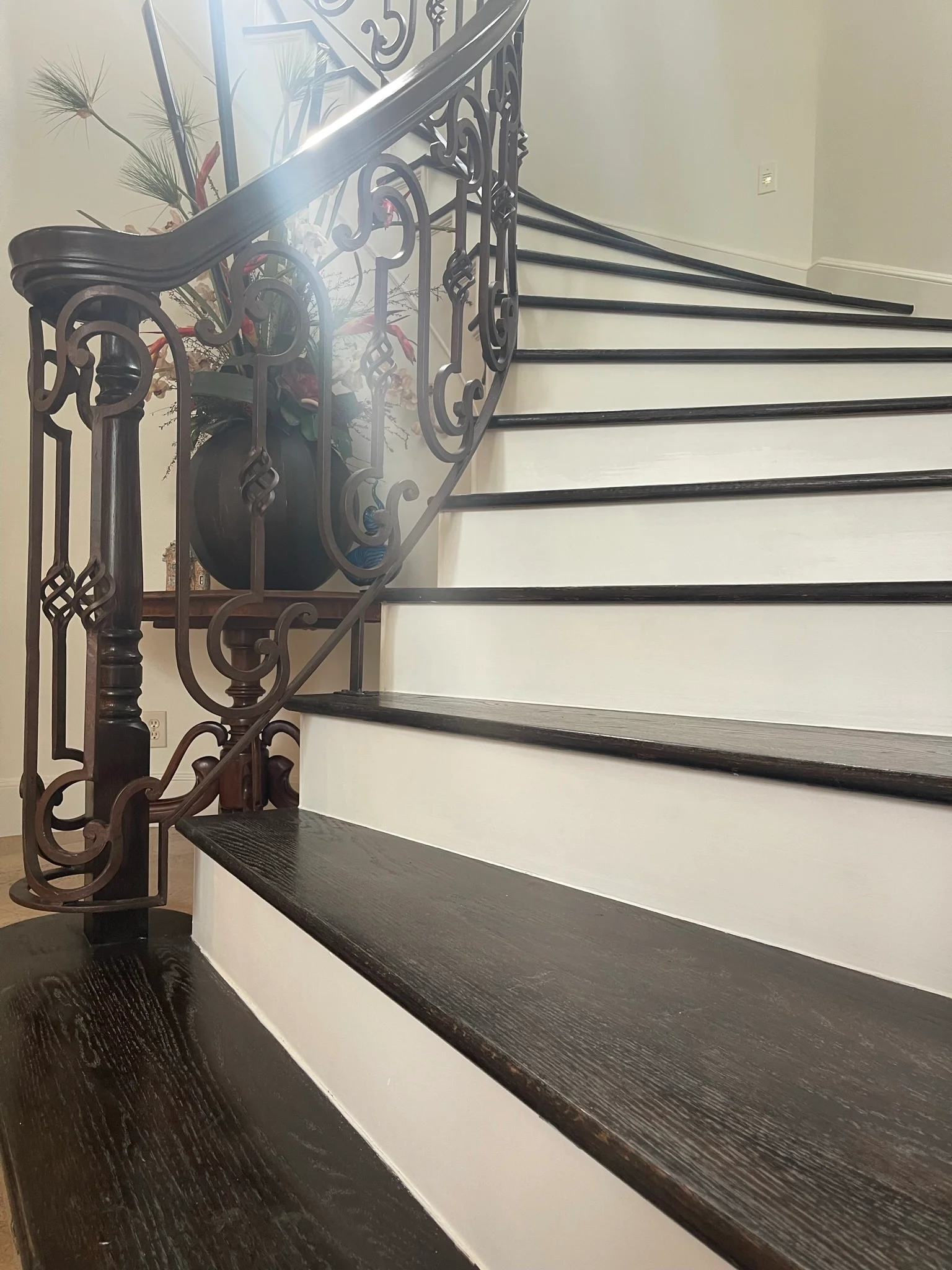 Black wrought iron stair railing with ornate scrollwork against white walls and dark wood stairs