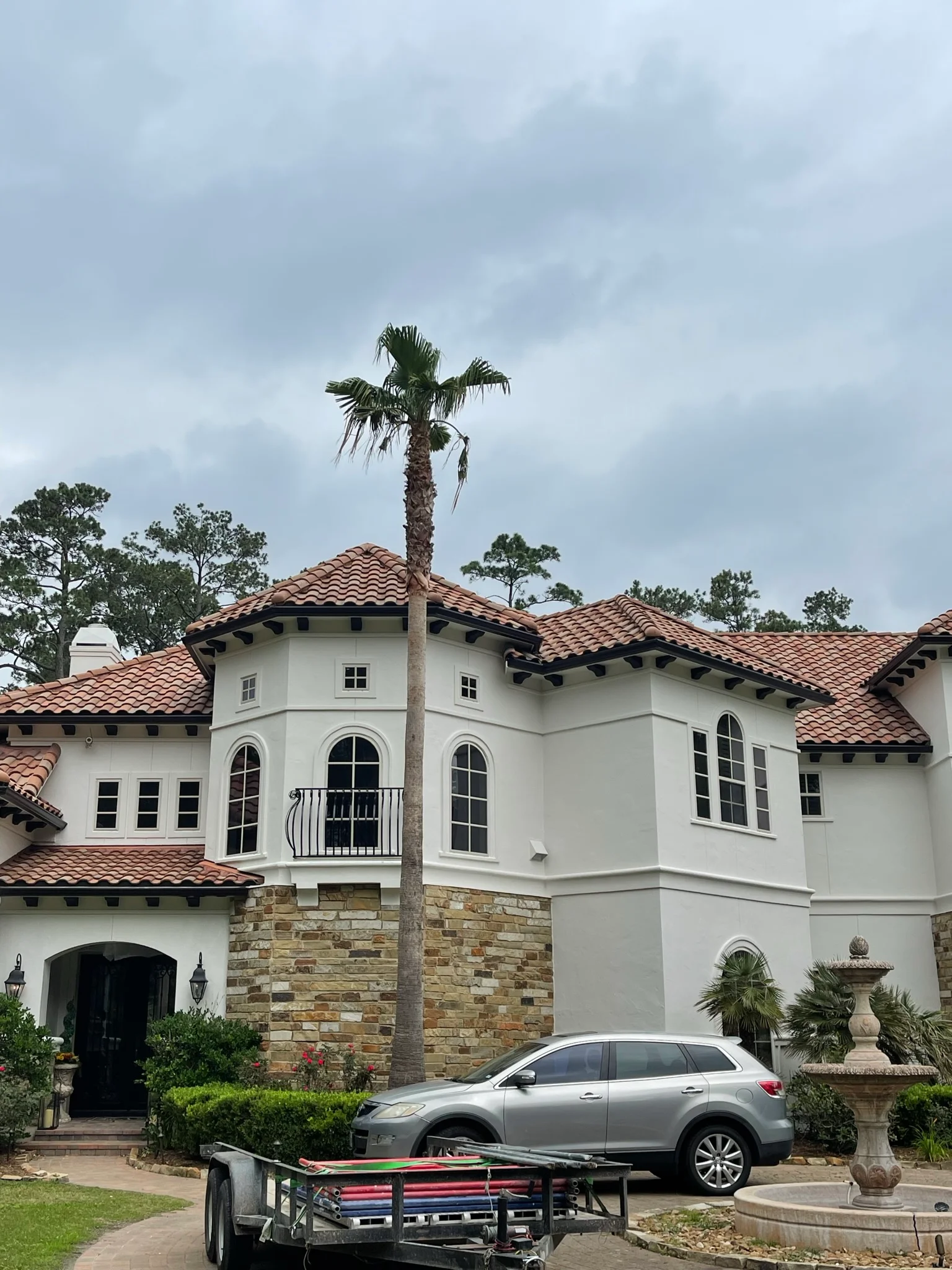Spanish Colonial home with white stucco, terracotta tile roof, stone base, and palm tree